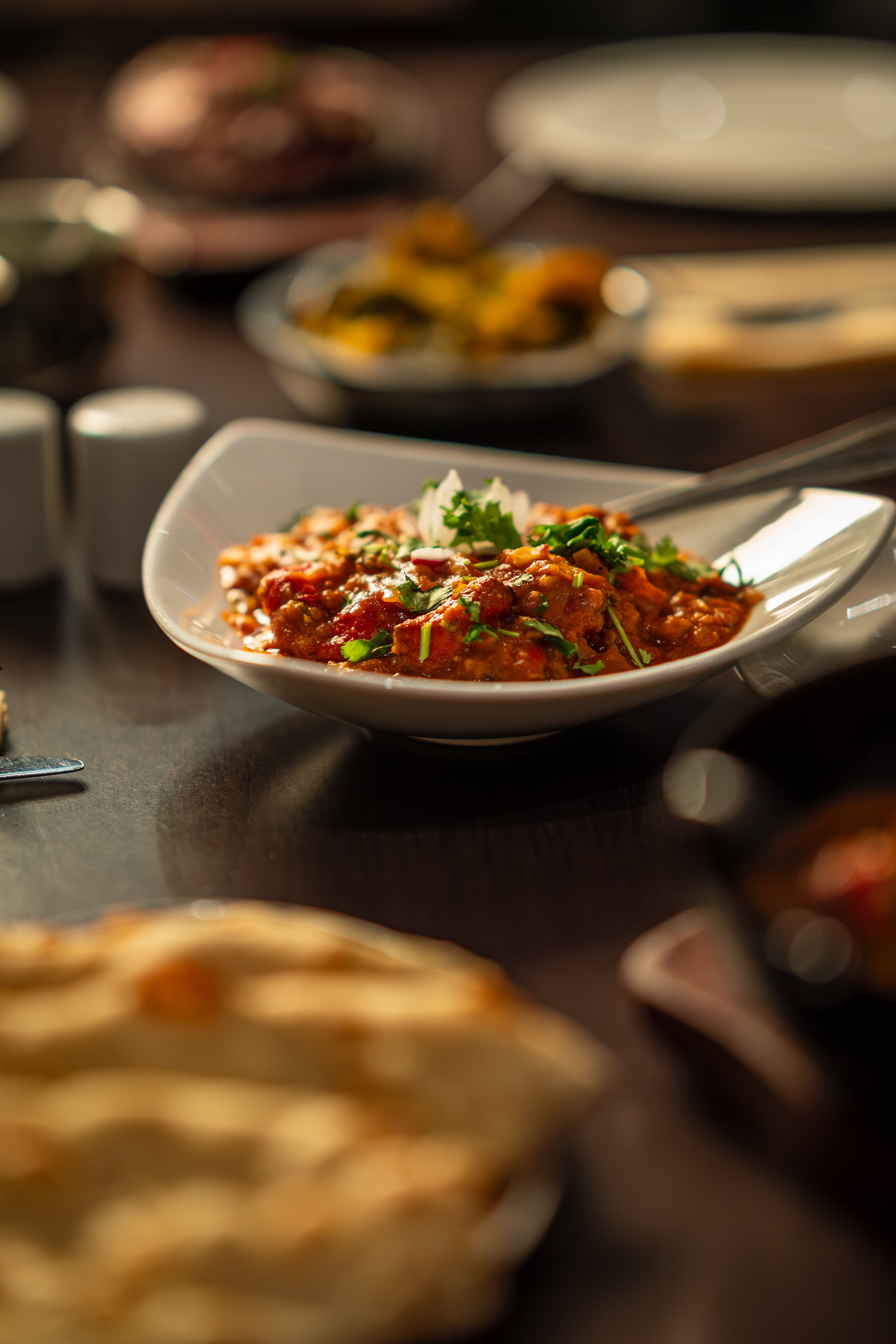 Curry in a white bowl with naan and side dishes