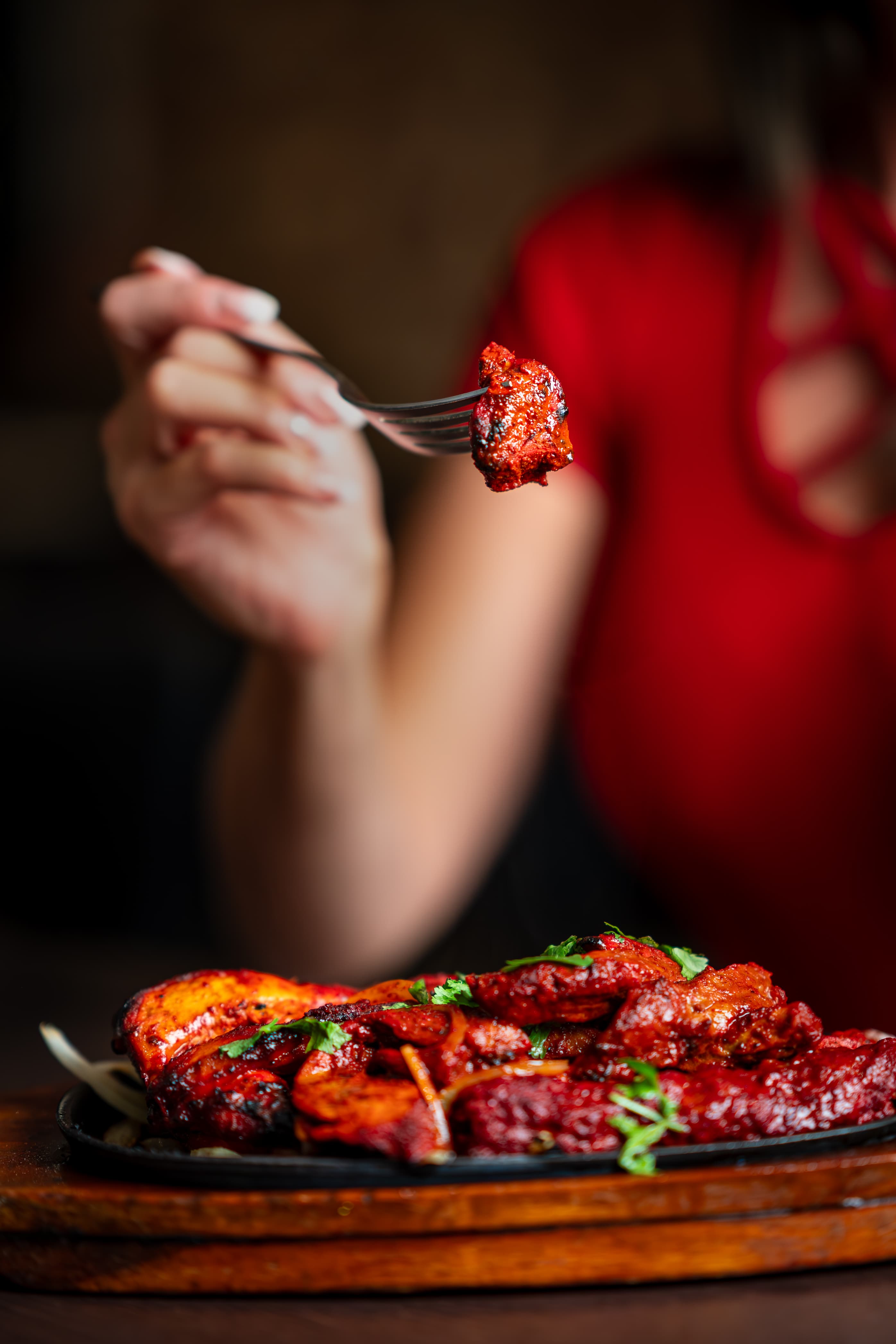 Piece of chicken tikka on a fork above the sizzler